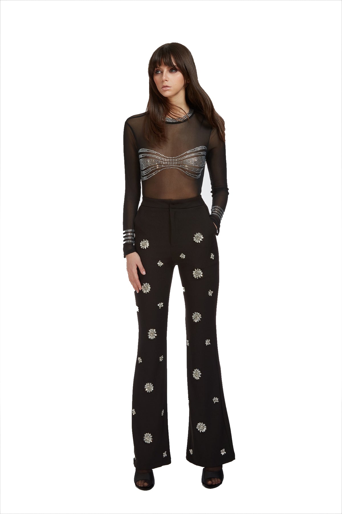 A model wearing a black sheer long-sleeve top with a metallic silver corset-style waist overlay and black flared pants with white floral embroidery, set against a plain white background.