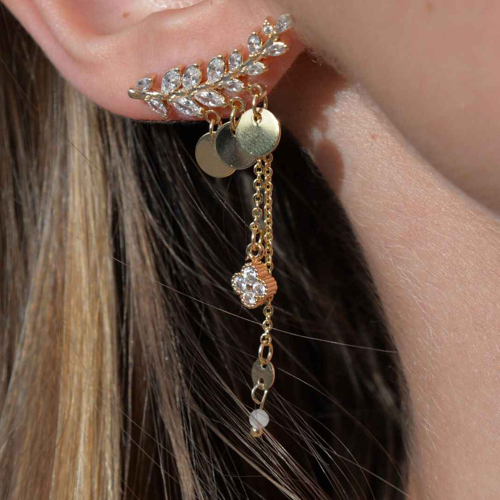 Gold earring with leaf design and dangling beads worn by a person.
