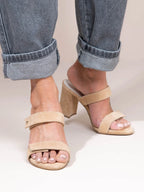 Beige sandals worn with rolled-up jeans on a neutral background