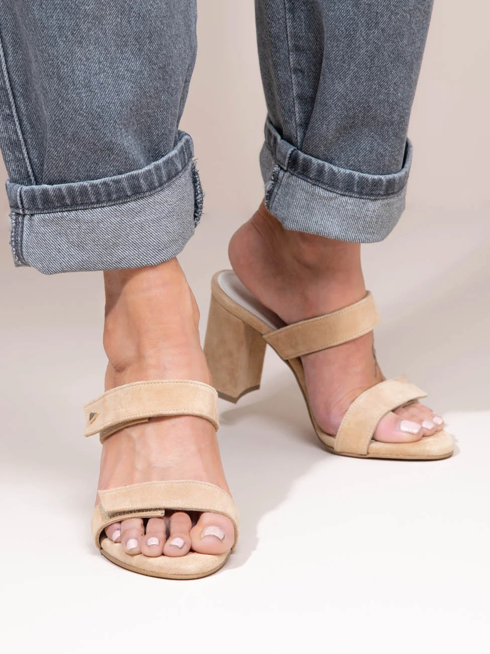 Beige sandals worn with rolled-up jeans on a neutral background