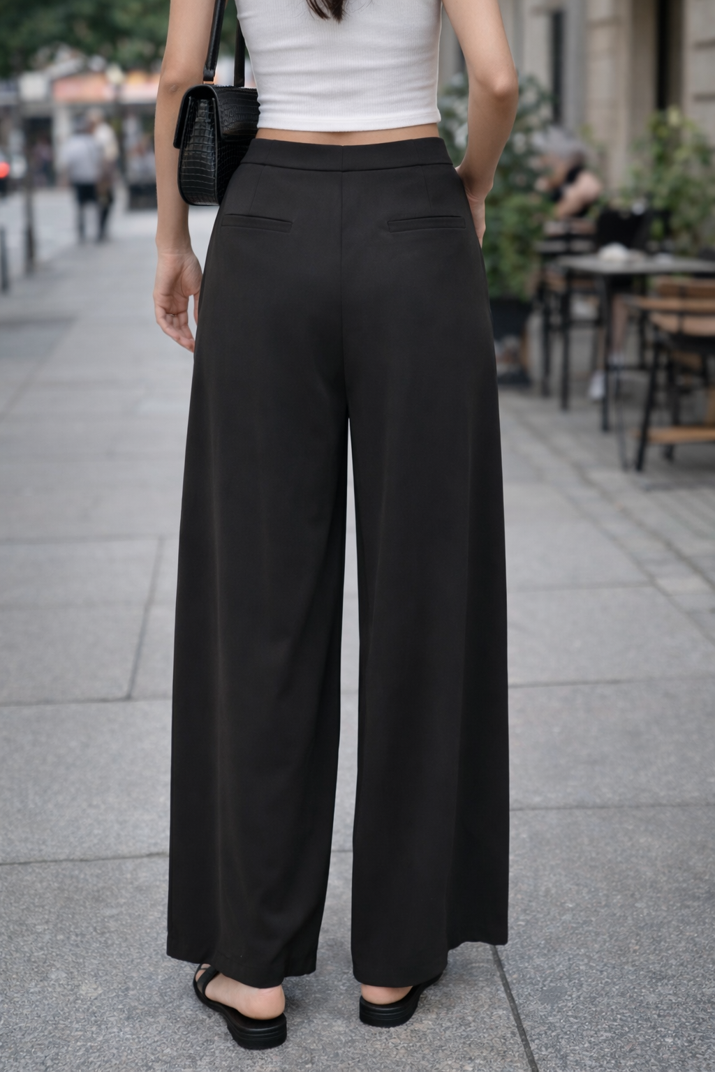Person wearing black wide-leg pants and a white top on a city street.