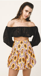 Woman wearing a black off-shoulder top and a colorful skirt with sunflower pattern on a white background