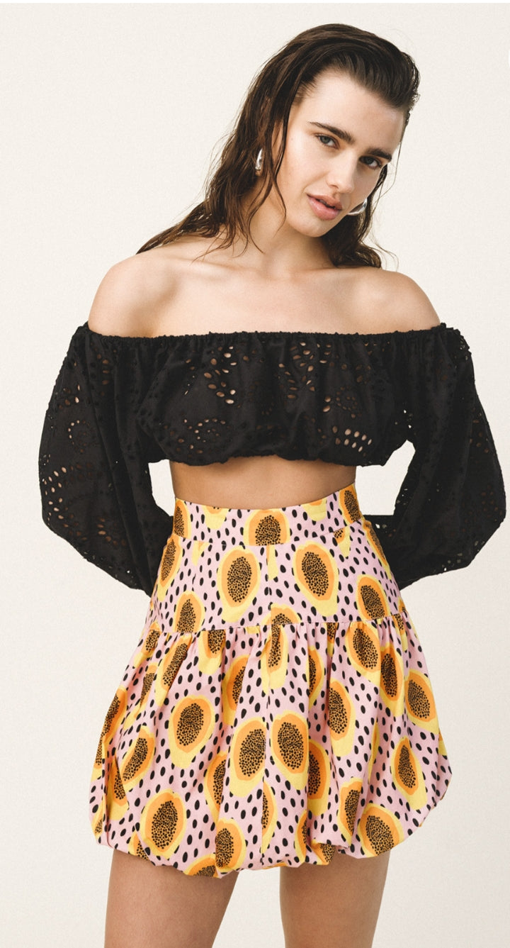 Woman wearing a black off-shoulder top and a colorful skirt with sunflower pattern on a white background