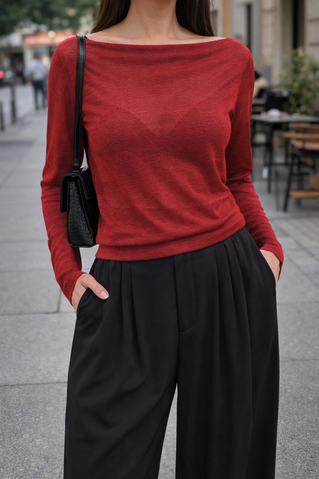 Person wearing a red sweater and black pants on a city street.
