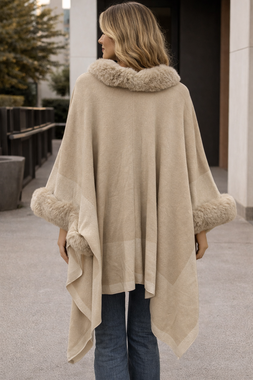 Woman wearing a beige poncho with fur trim in an outdoor setting