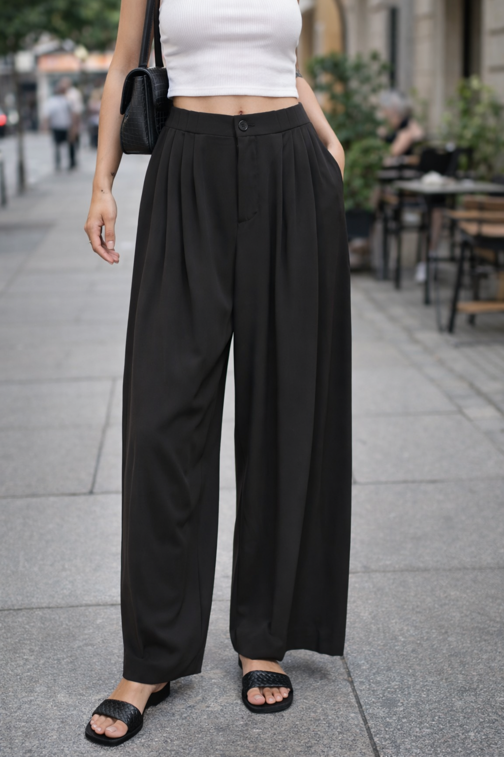 Person wearing black wide-leg pants and a white top on a city street.