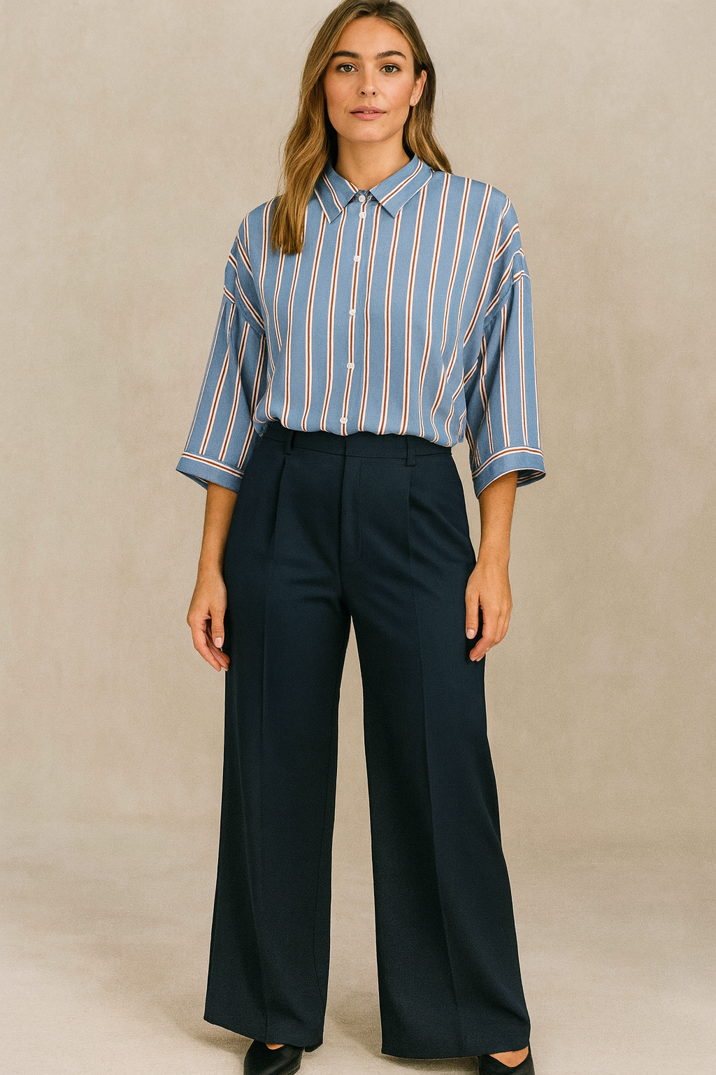 Woman wearing a blue striped shirt and navy pants against a beige background