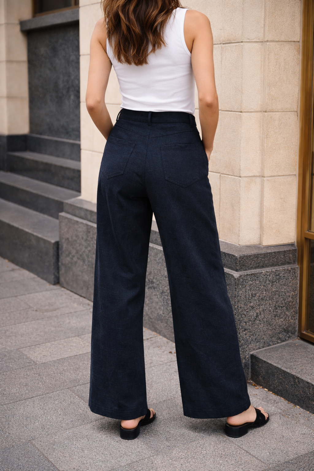 Person wearing navy pants and a white top standing on a sidewalk.