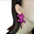 Pink lizard-shaped earring worn by a person with dark hair.
