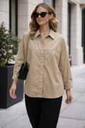 Woman wearing a beige shirt and black pants on a city street.