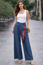 Woman wearing a white tank top and blue wide-leg pants with a red scarf, standing on a city street.