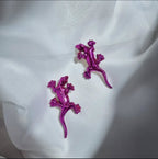 Purple lizard-shaped earrings on a white fabric background