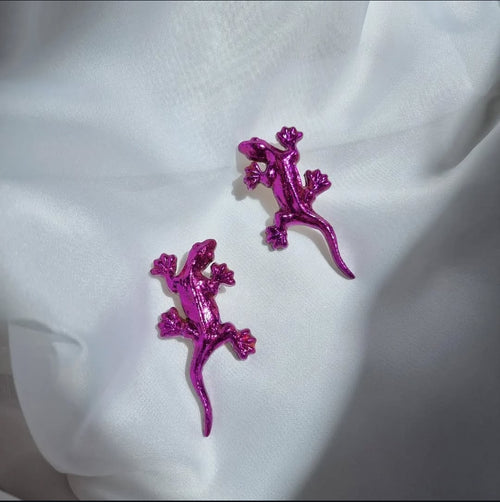 Purple lizard-shaped earrings on a white fabric background