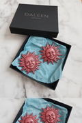 Sun-shaped earrings in a black Daleen jewelry box on a marble surface