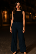 Woman wearing a black sleeveless top and navy pants against a dark background