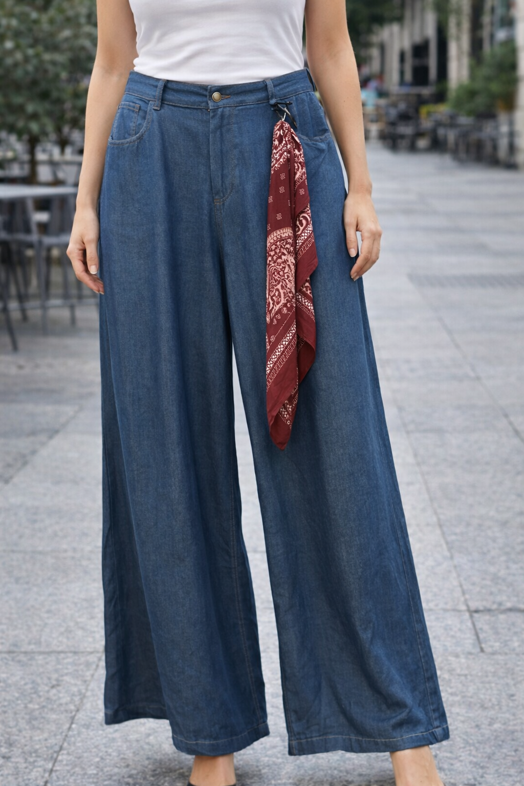Person wearing wide-leg jeans with a red patterned scarf, standing on a city street.