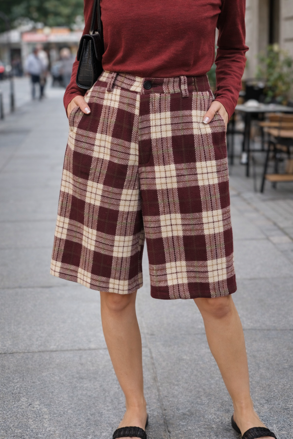 Person wearing plaid shorts and a red top on a street.