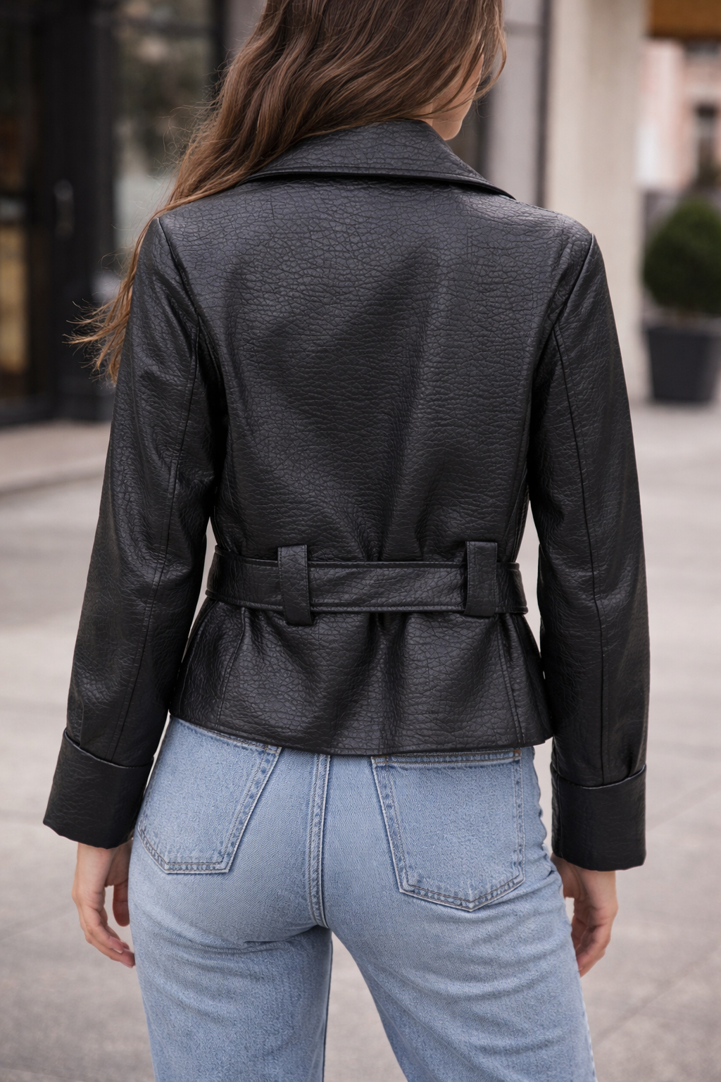 Person wearing a black leather jacket with a belt, standing outdoors.