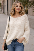 Woman wearing a cream sweater and blue jeans on a street.