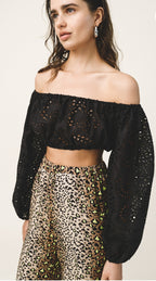 Woman wearing a black off-shoulder top with sheer sleeves and leopard print pants on a light background