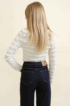 Person wearing a white textured long-sleeve top and dark jeans on a beige background