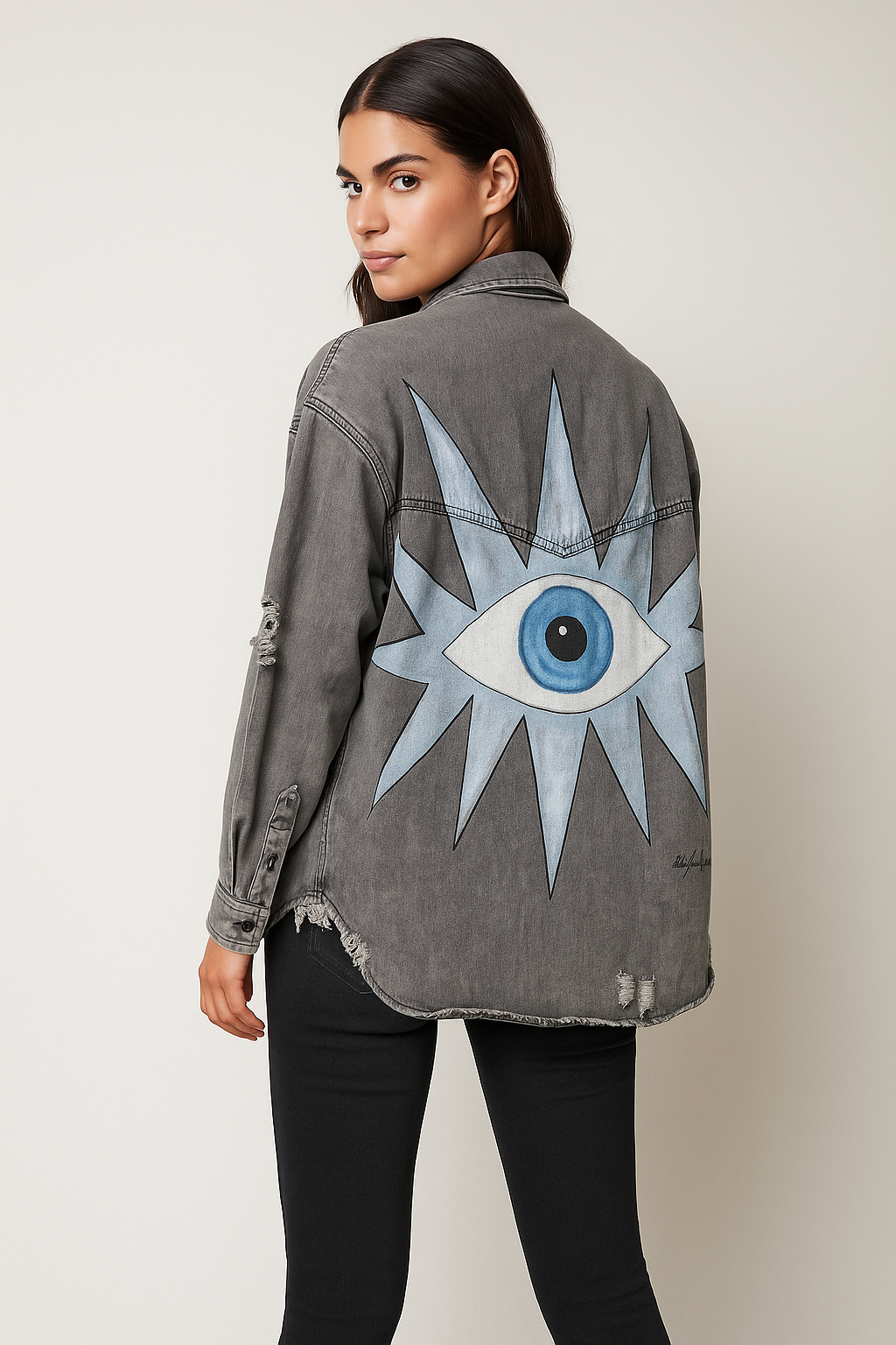 Person wearing a gray denim jacket with a blue eye design on the back against a plain background