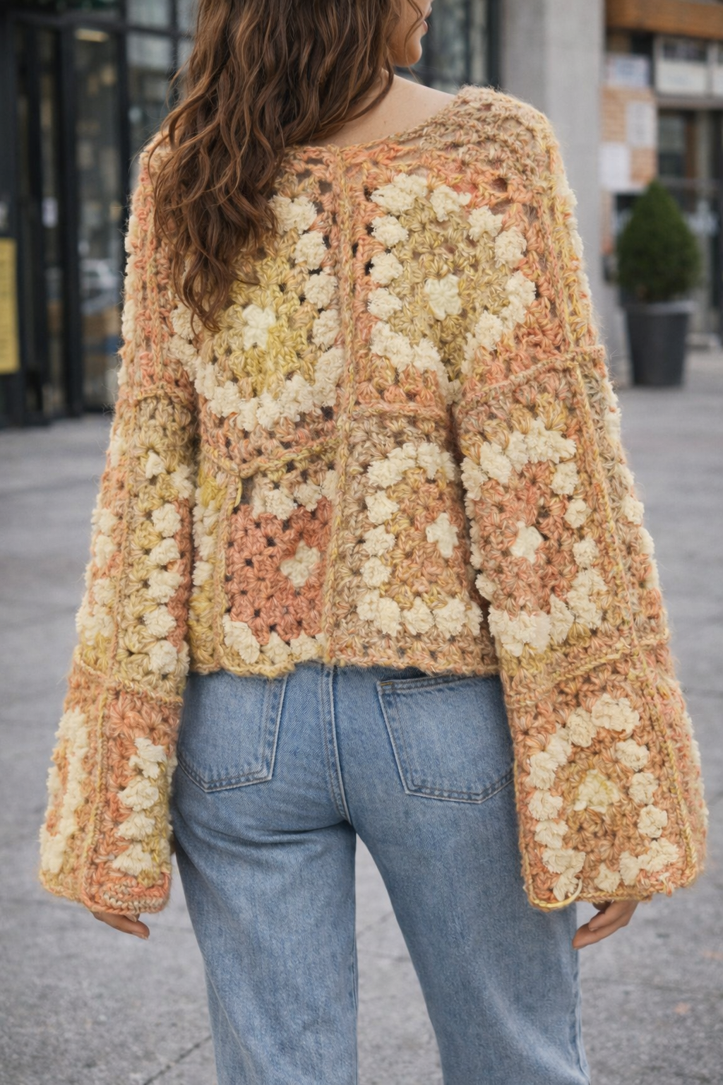 Person wearing a patterned crochet sweater and jeans outdoors.