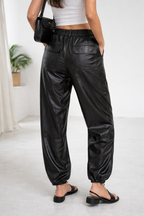 Person wearing black leather jogger pants and a white top in a minimal indoor setting.