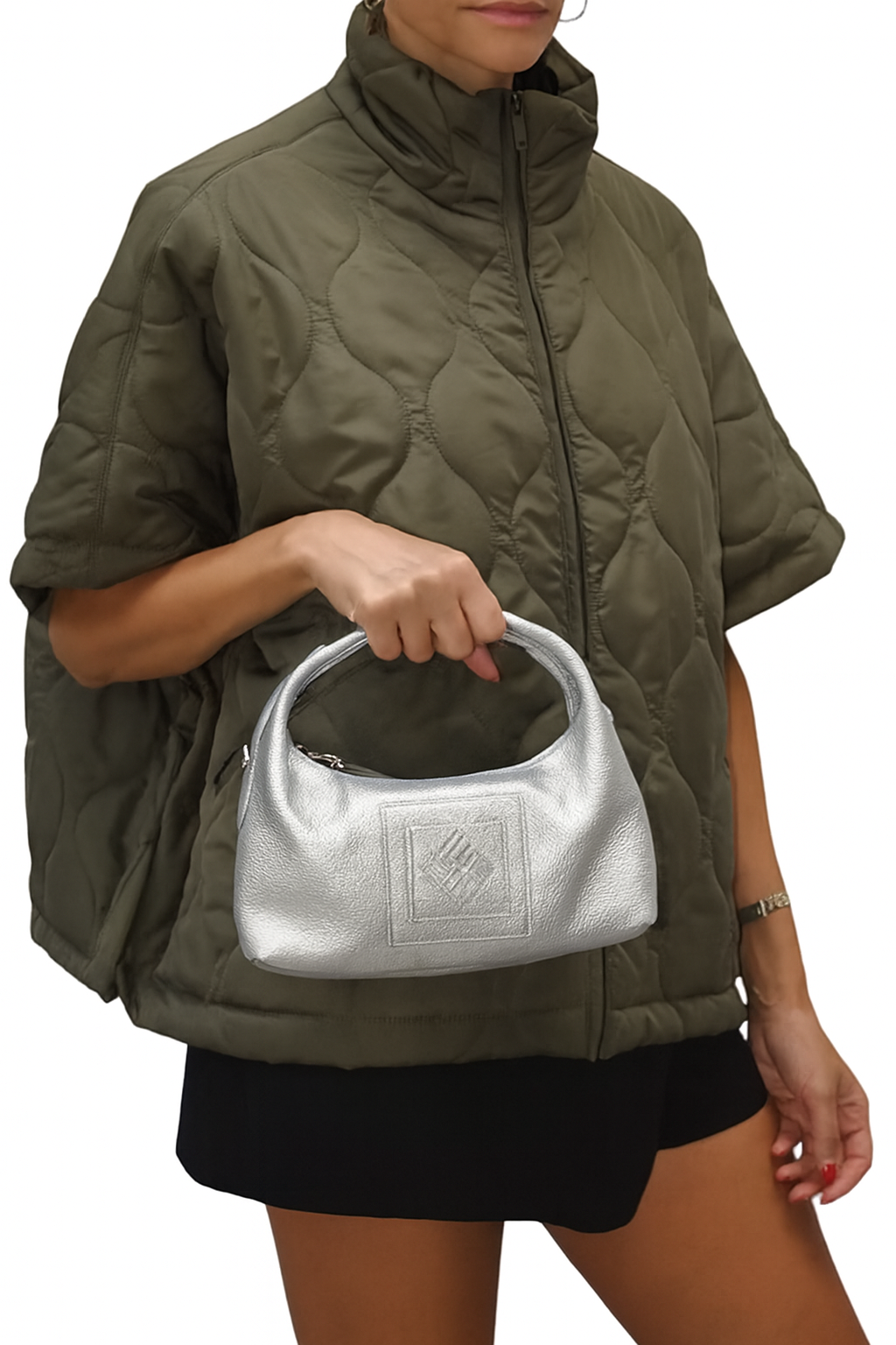 Person wearing a green quilted jacket holding a silver handbag on a white background