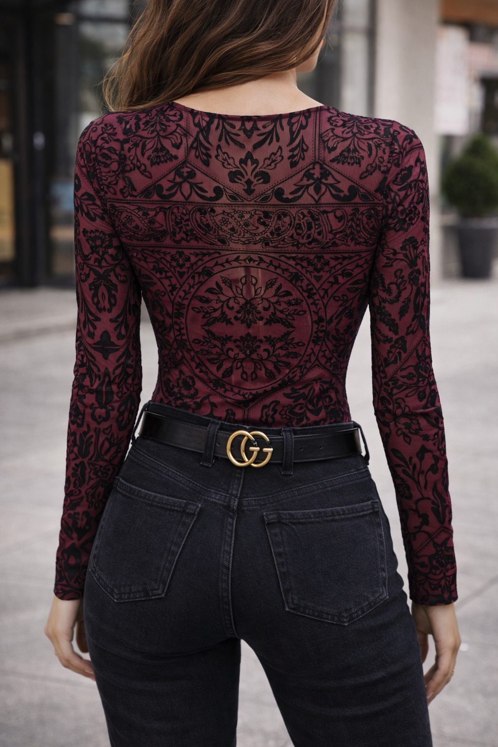 Person wearing a burgundy lace long-sleeve top and black pants with a Gucci belt.