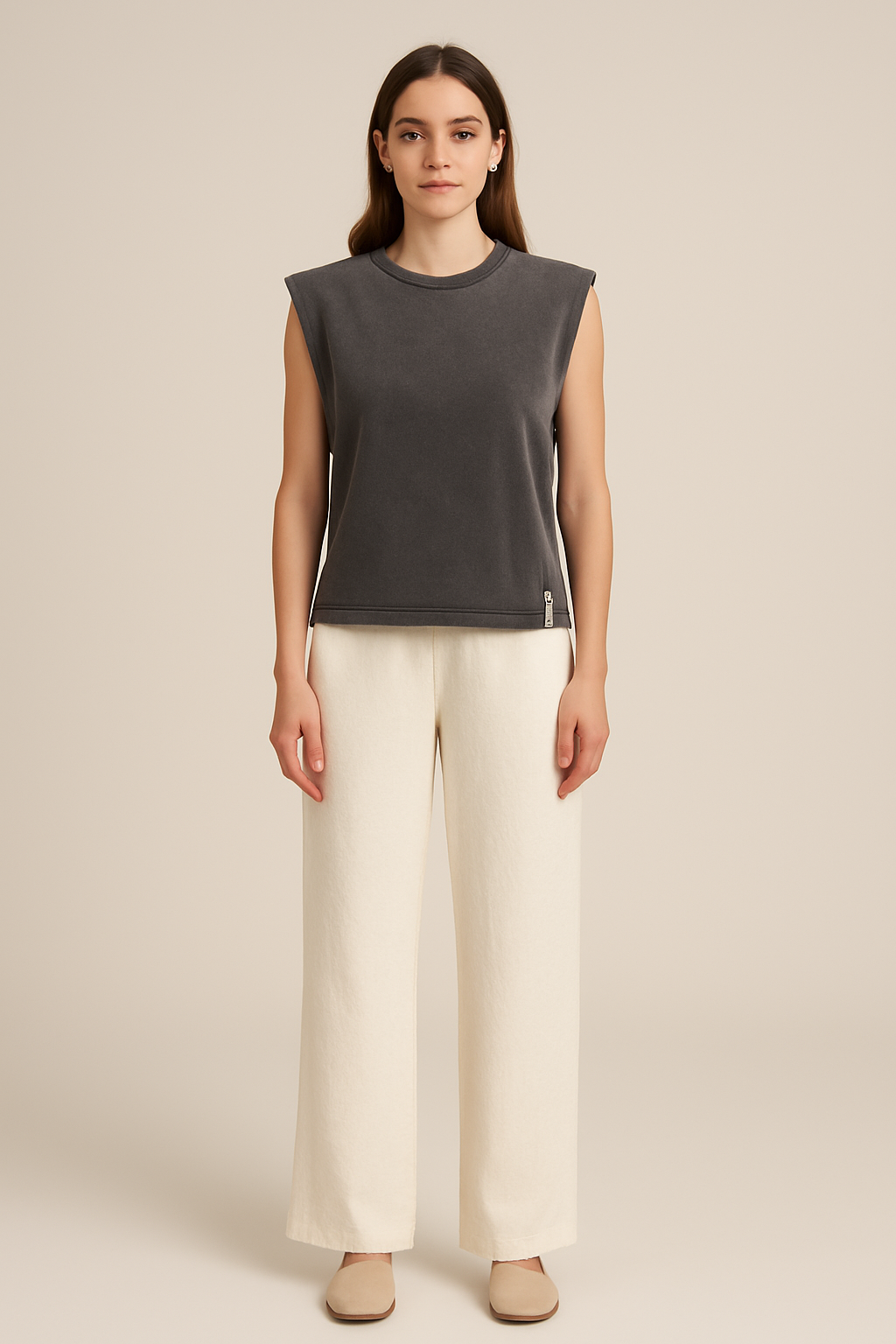 Woman wearing a dark gray sleeveless top and white pants on a beige background