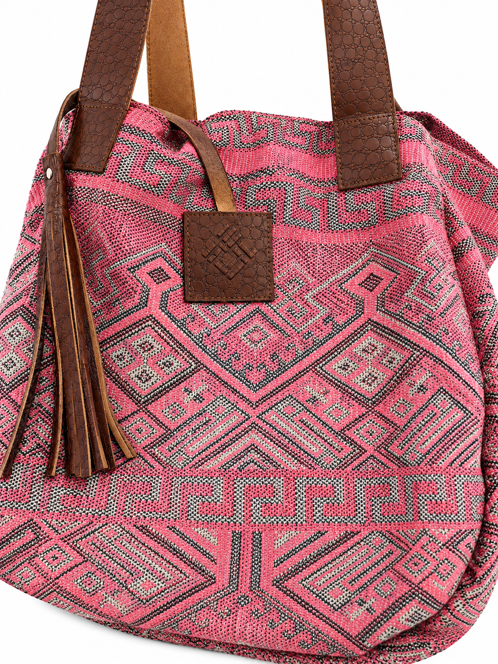 A pink woven tote bag with a geometric pattern and brown faux-leather straps, featuring a tassel and a front leather patch.