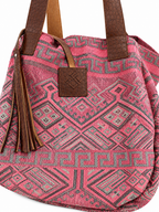 A pink woven tote bag with a geometric pattern and brown faux-leather straps, featuring a tassel and a front leather patch.