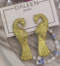 Gold fish-shaped earrings on a Daleen jewelry card with a marble surface.