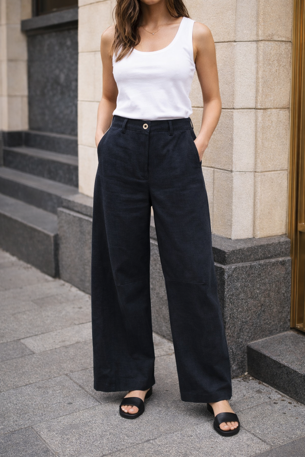 Person wearing a white tank top and black wide-leg pants standing on a sidewalk.