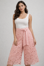 Woman wearing a white sleeveless top and pink lace pants on a gray background