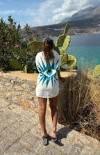 Person wearing a white "Eye" See You Jacket with a blue design, standing on a stone path with cacti and a scenic background.