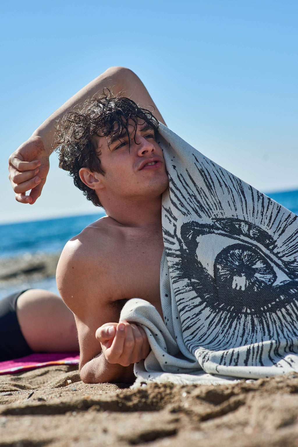 Man lying on a beach with a towel draped over his shoulder, ocean in the background