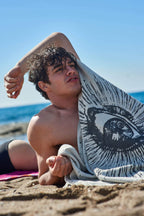 Man lying on a beach with a towel draped over his shoulder, ocean in the background