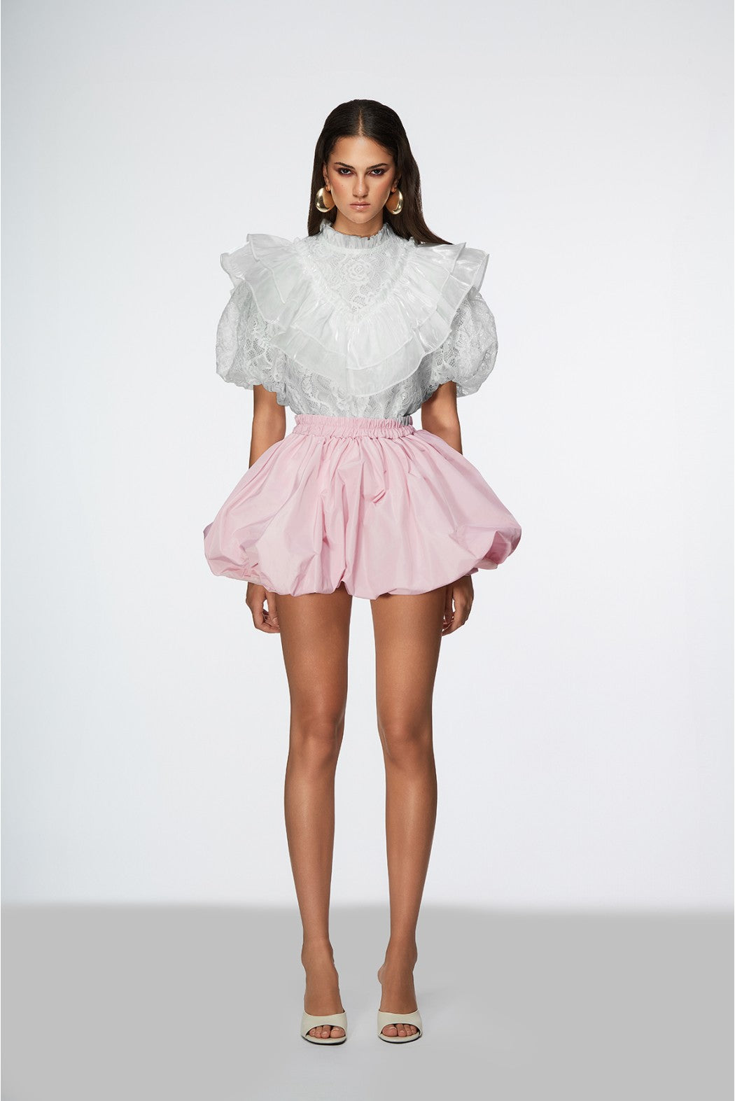 Woman wearing a white ruffled top and pink skirt on a white background