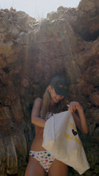 Woman sitting among rocks holding a white bag with text