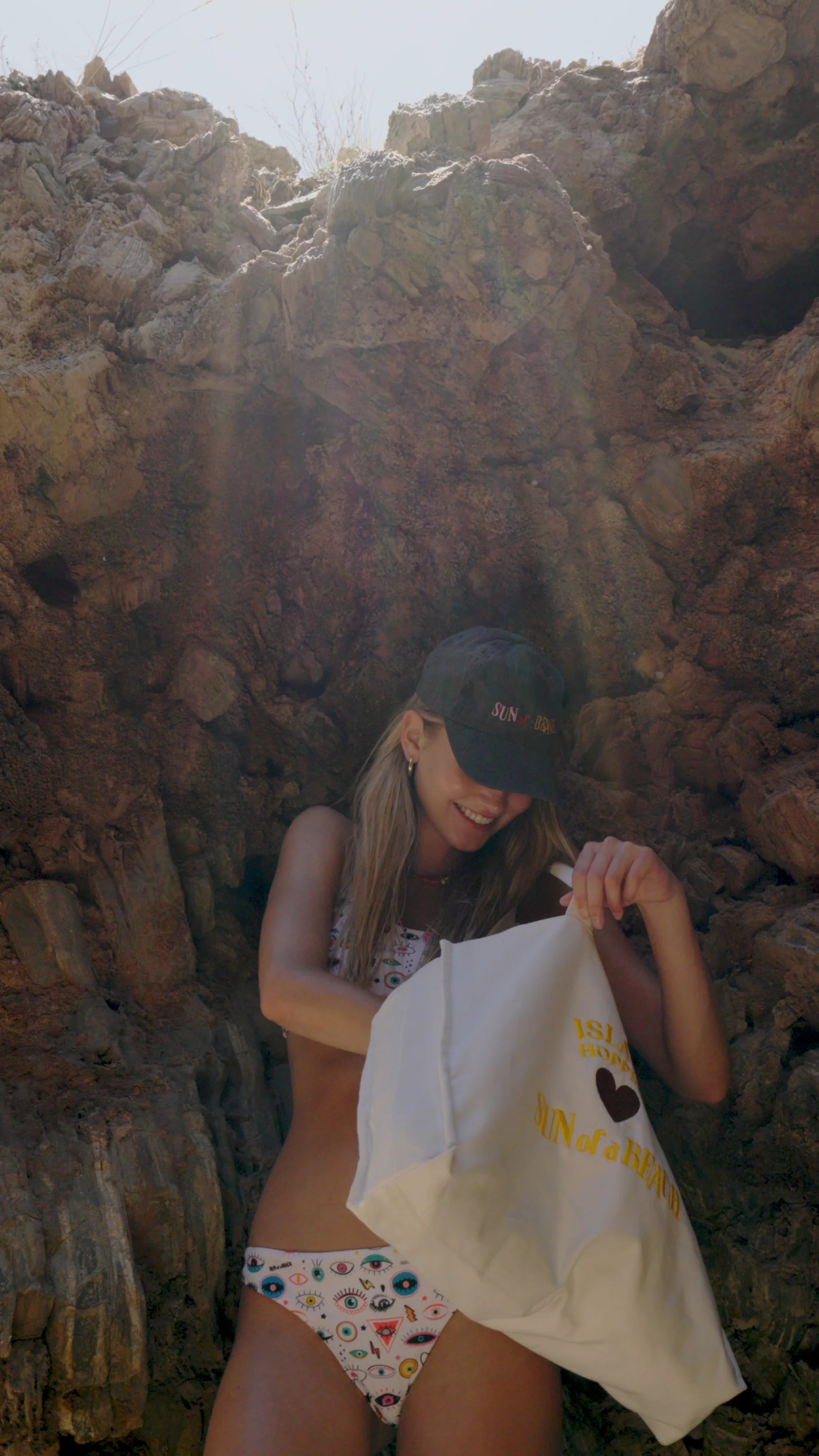 Woman sitting among rocks holding a white bag with text