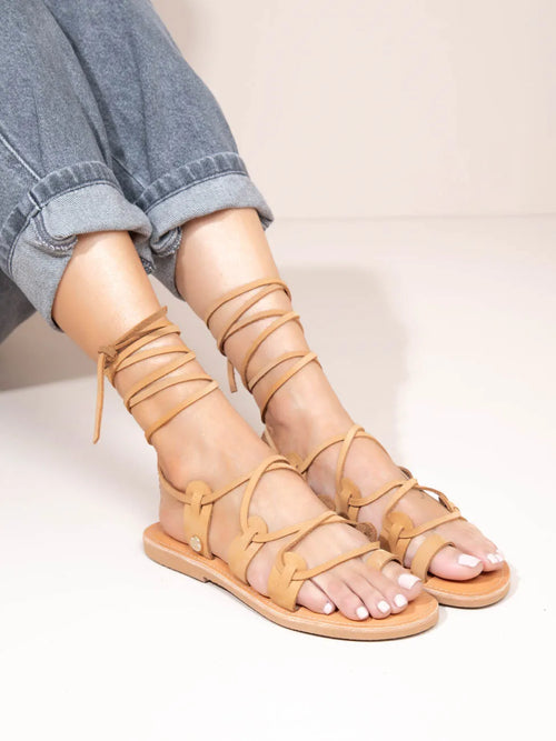Beige strappy sandals worn with rolled-up jeans on a neutral background