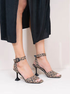 Leopard print high-heeled shoes worn with a black outfit on a white background