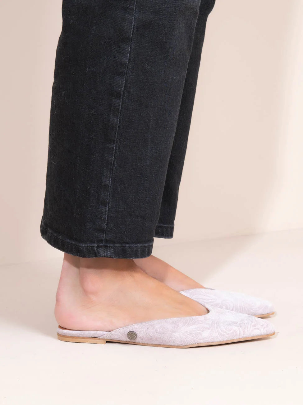 Person wearing black pants and white slippers on a beige background