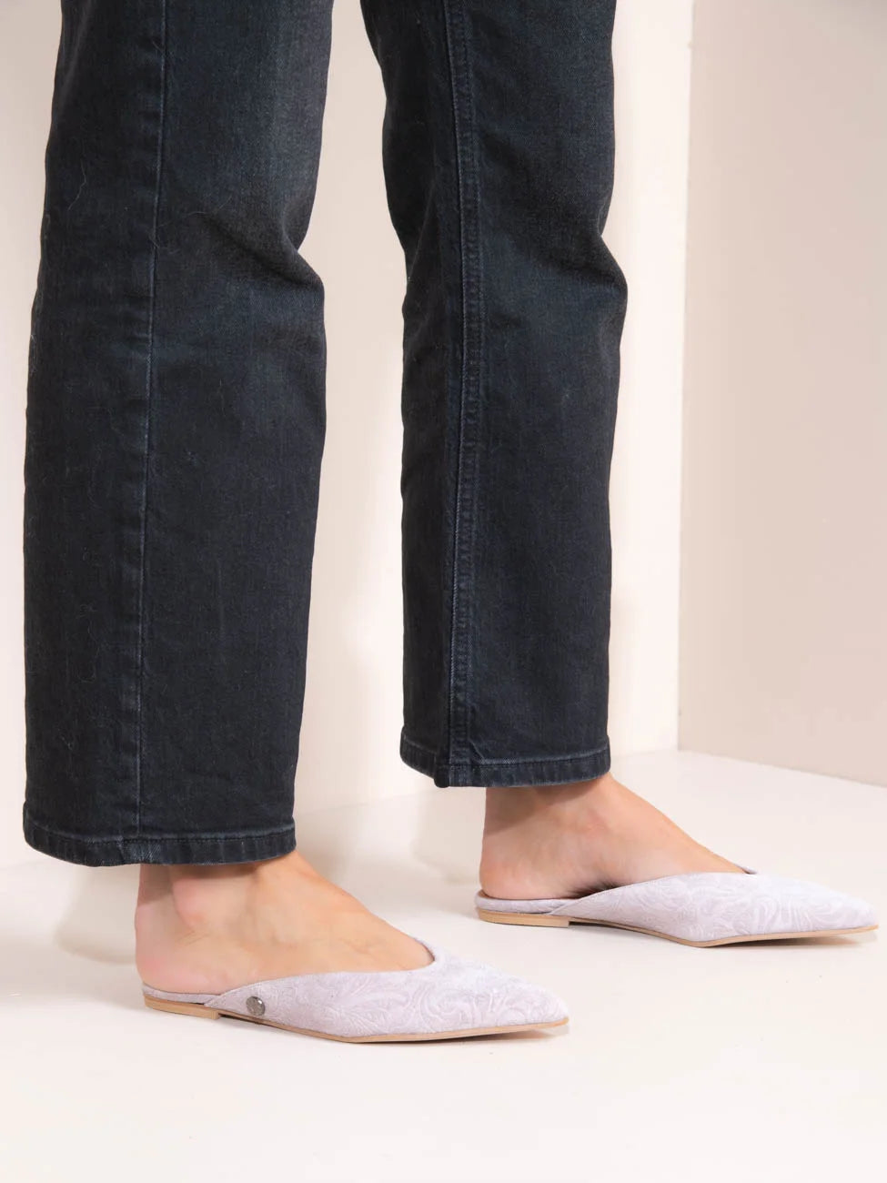 Person wearing dark jeans and light gray flats on a plain background