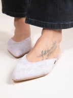 White pointed-toe flats worn with black jeans on a light background