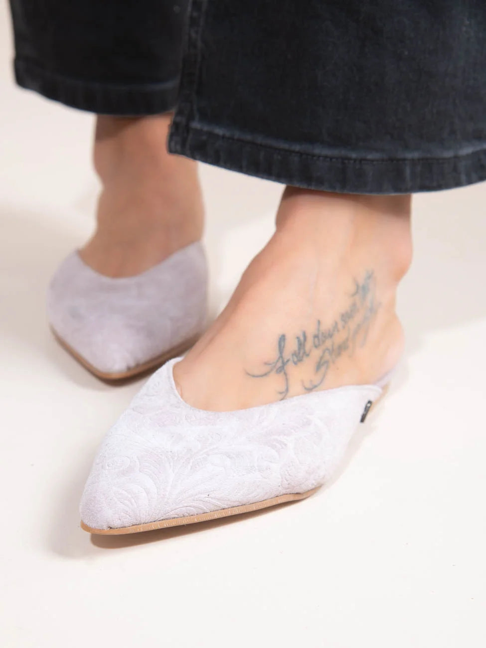 White pointed-toe flats worn with black jeans on a light background