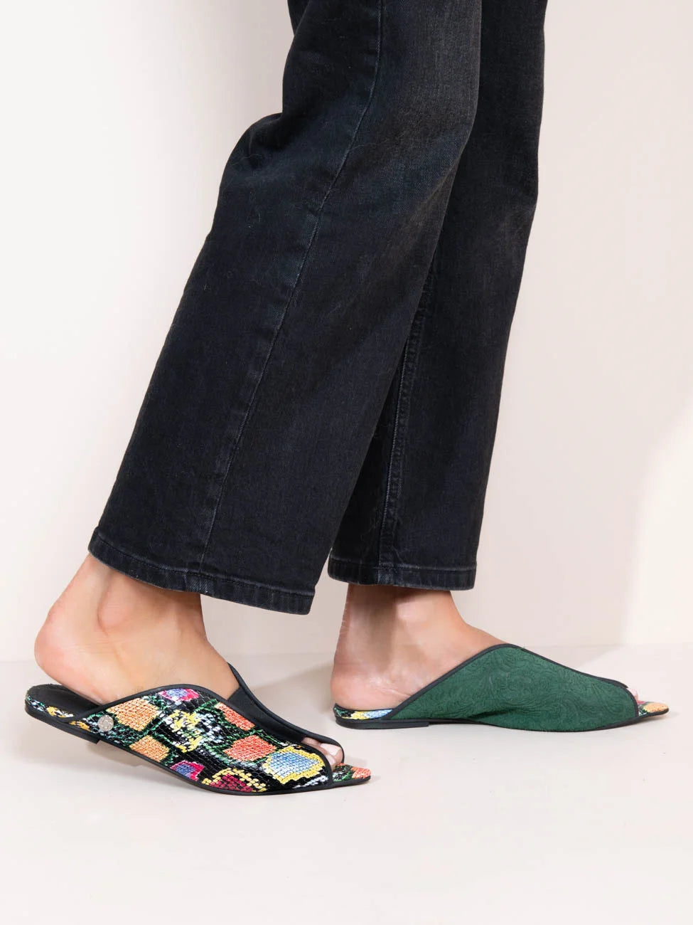 Person wearing floral slippers and green open-toe shoes on a plain background