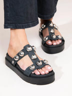 A pair of black sandals with a metallic sole and multiple straps with round beads on a person's feet.